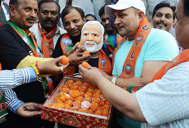 Indian supporters offer sweets to another wearing a mask of the newly sworn-in Indian Prime Minister Narendra Modi. AFP