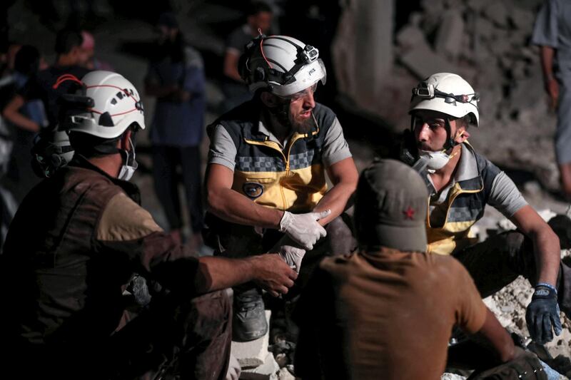 Members of the Syrian Civil Defence, also known as the "White Helmets", wait by as their comrades clear debris while searching for bodies or survivors in a collapsed building following a reported government air strike in the village of Saraqib in Syria's northwestern Idlib province.  AFP