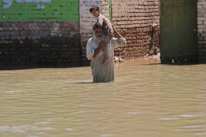 A man holding a baby wades through a flooded area in Khyber Pakhtunkhwa province. EPA