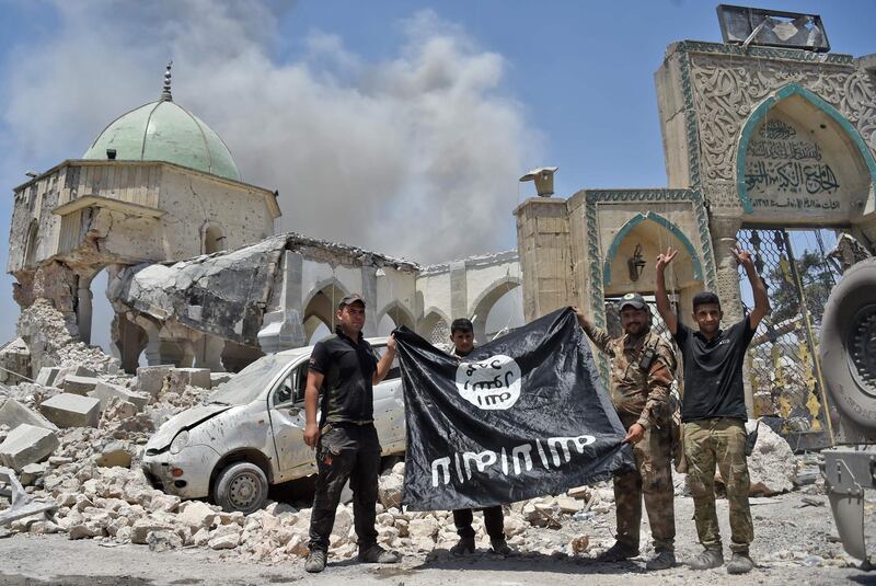 (FILES) In this file photo taken on June 30, 2017, members of the Iraqi Counter-Terrorism Service (CTS) with a flag of the Islamic State held upside-down, outside the destroyed Al-Nuri Mosque in the Old City of Mosul, after the area was retaken from IS. Even as the last pockets of resistance in eastern Syria hold their ground, the Islamic State group is shapeshifting into a new, but no less dangerous, underground form, experts warn. Also known as ISIS, or the Islamic State in Iraq and Syria, it had long been ready to cede the territory it once held in its self-styled "caliphate," and has already begun the switch to a more clandestine role, closer to its roots.  / AFP / FADEL SENNA / TO GO WITH AFP STORY by Michel MOUTOT, "Islamic State not defeated, just transforming, experts say"
