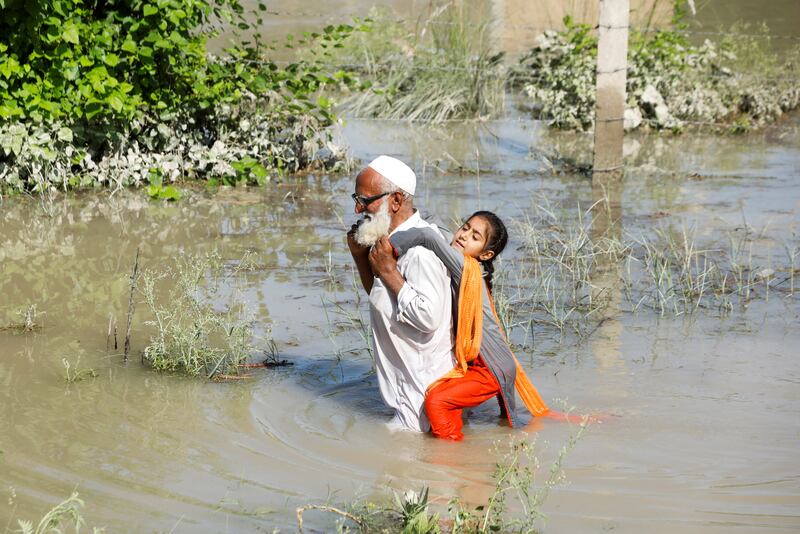 A man wades through floodwater carrying his granddaughter on his back in Charsadda. Reuters