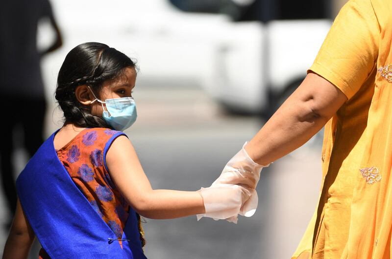 A mother and daughter, wearing protective gloves and face masks, walk together in the Emirate city of Dubai on March 31, 2020, after the country imposed a sweeping crackdown, closing its borders and halting passenger flight among others measures to contain the virus. The UAE, which takes in seven emirates including Dubai, has reported 611 coronavirus cases along with five deaths.  / AFP / KARIM SAHIB
