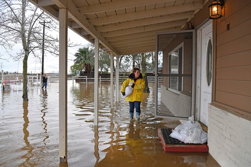 A woman carries a sand bag to her flooded home in Brentwood. AP
