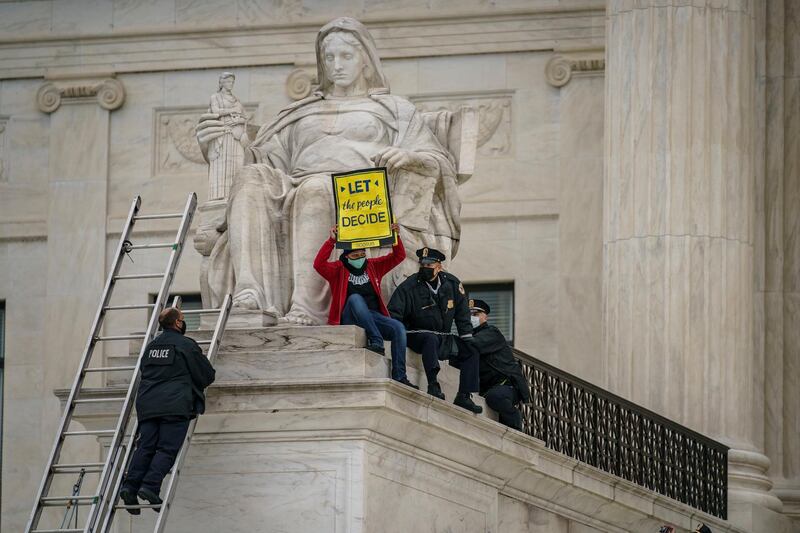 A protester opposed to the Senate's race to confirm Amy Coney Barrett is removed by police after chaining themselves to a railing and holding a sign while sitting atop the statue Contemplation of Justice, at the Supreme Court building in Washington. AP Photo