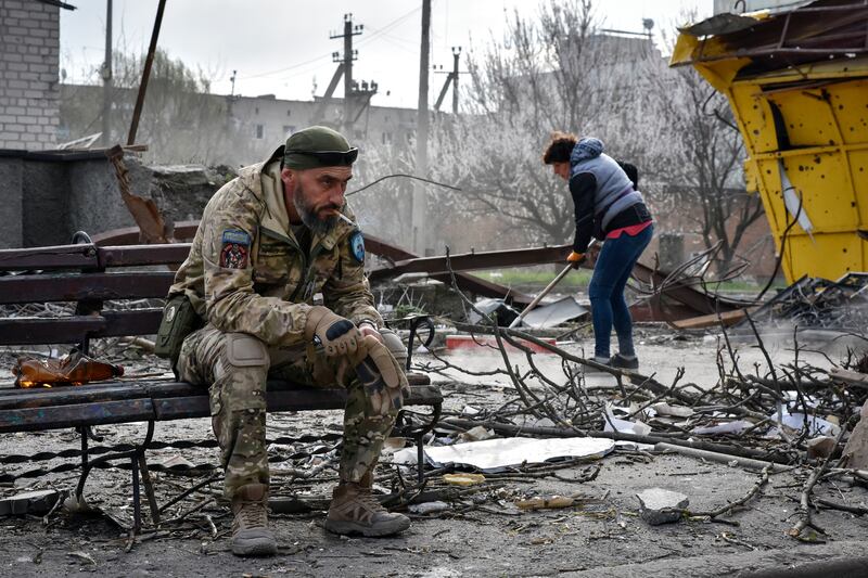 A Ukrainian soldier rests as a resident clears debris near a building damaged in a Russian strike in the town of Orikhiv, Zaporizhzhia region. AP