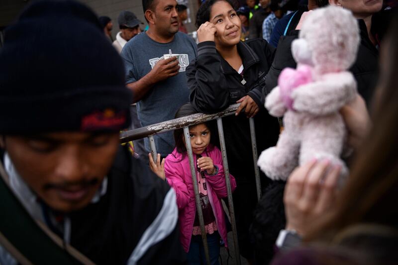 A girl from Honduras waits for a present given by a nongovernmental organization outside an empty warehouse used as a shelter set up for migrants in downtown Tijuana, Mexico, Tuesday, Dec. 25, 2018. Critics, including former allies and some of the migrants themselves, say Pueblo Sin Fronteras, a group of activists escorting the caravan called in English, "People Without Borders," downplayed the dangers of Central Americans' treks toward the United States, especially for families and small children, and misled the participants about how long they would have to wait on the Mexican side to apply for asylum. (AP Photo/Daniel Ochoa de Olza)