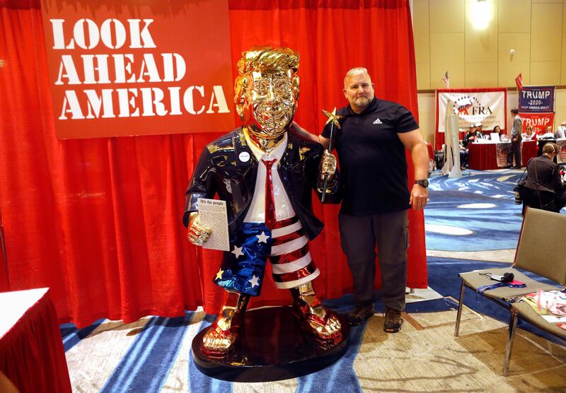 A conference attendee poses next to a statue of Donald Trump. Artist Tommy Zegan says the statue's US flag-themed shorts symbolise that the former president is a patriot. Reuters