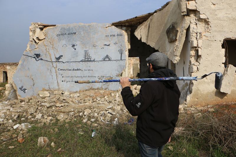 Al Shami holding a roller brush looking at the mural 'Syria Game'. The mural appears on a ruined roof. Abd Almajed Alkahr/The National