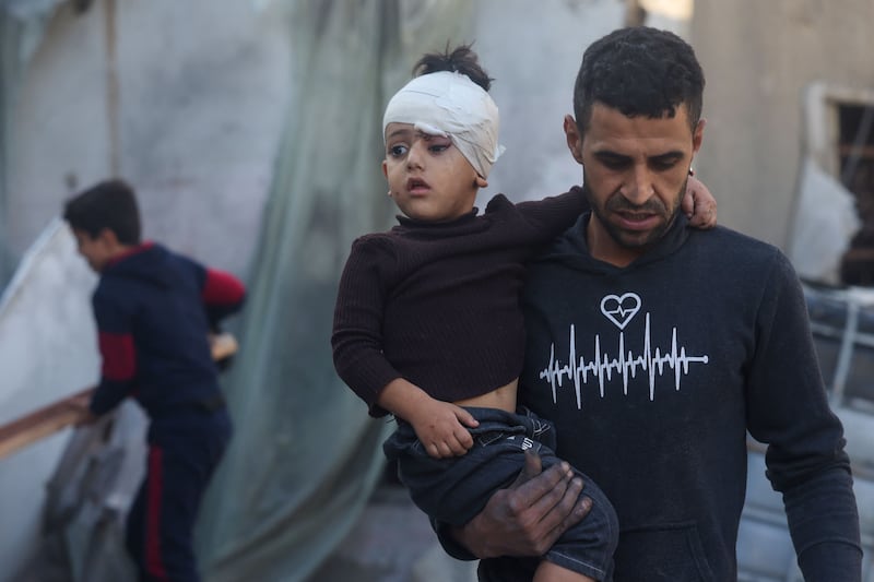 A Palestinian man carries a child injured during Israeli bombardment in Rafah. AFP