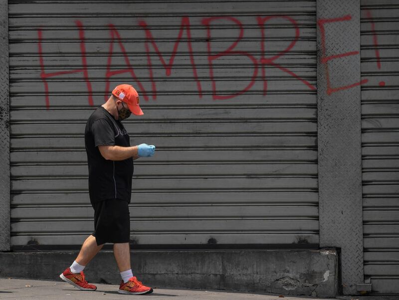 A man wearing a face masks, as a preventive measure against the spread of the new coronavirus, COVID-19, walks by a graffiti reading "Hunger", in Caracas.  AFP