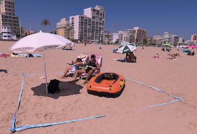 (FILES) In this file photo taken on July 01, 2020 People use a barrier tape to set a secure social distance space at the Nord Beach in Gandia, near Valencia on July 1, 2020. Spain will allow all vaccinated travellers to visit the country from June 7, Prime Minister Pedro Sanchez said on May 21, 2021, as the tourism hotspot aims to revive its virus-battered travel industry. / AFP / JOSE JORDAN
