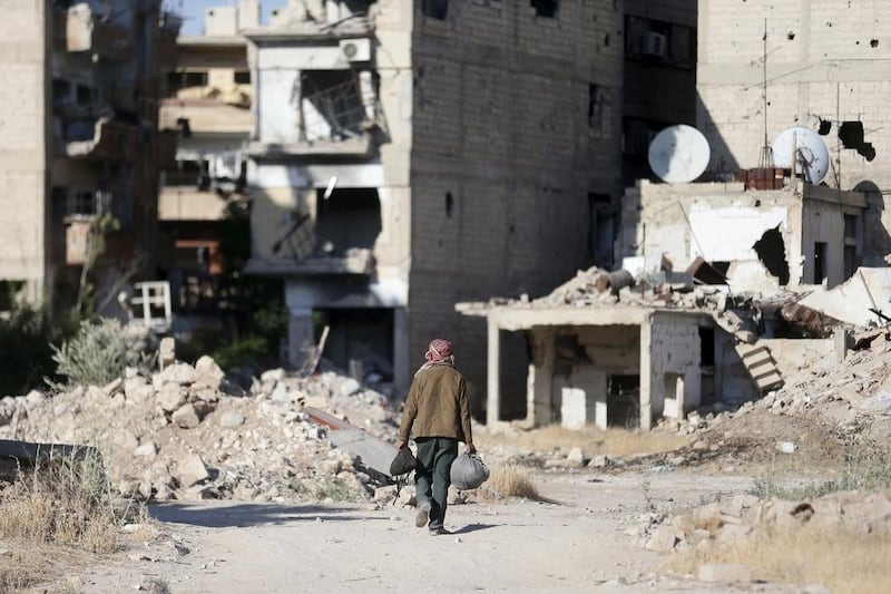 A man carries his belongings as he walks past damaged buildings along a street in Jobar, a suburb of Damascus. (REUTERS/Bassam Khabieh)