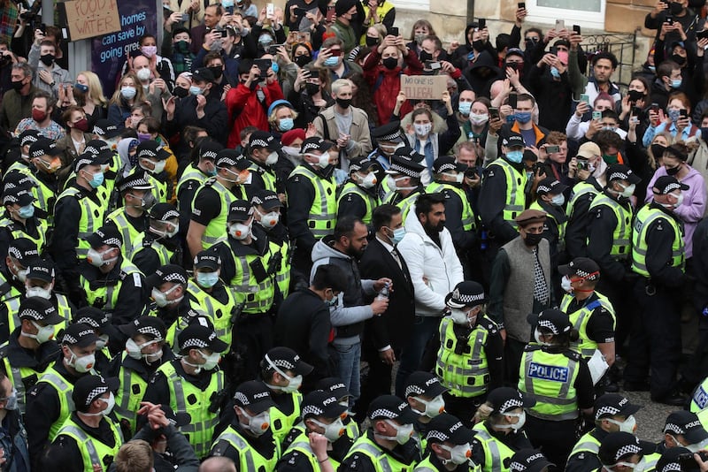 Two men stand surrounded by police and protesters, after being released from an Immigration Enforcement police van accompanied by lawyer Aamer Anwar and Mohammad Asif, director of the Afghan Human Rights Foundation, in Glasgow, Scotland, Thursday May 13, 2021.  Some hundreds of protesters blockaded the street in Glasgow on Thursday in a seven-hour standoff which successfully forced the release of two men detained by U.K. immigration authorities. (Andrew Milligan/PA via AP)