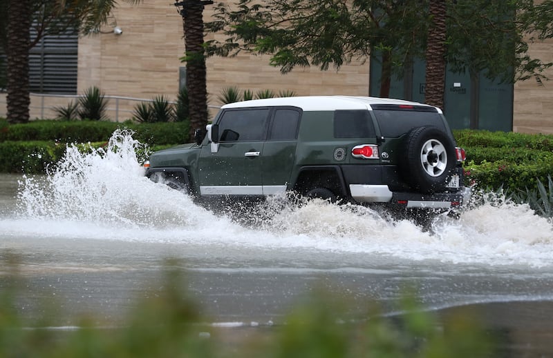 A vehicle drives through a flooded road on a wet day in Dubai. Chris Whiteoak / The National