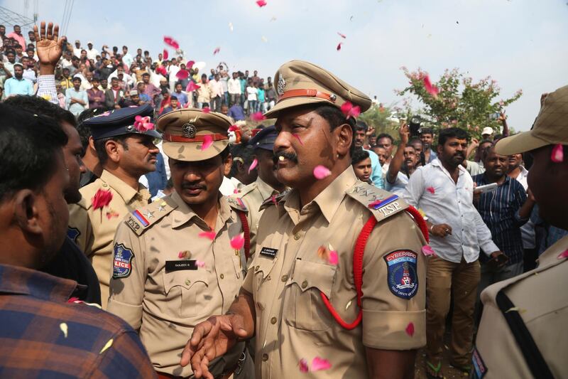 People throw flower petals on the Indian policemen guarding the area where rape accused were shot, in Shadnagar some 50 kilometers or 31 miles from  Hyderabad, India, Friday, Dec. 6, 2019. An Indian police official says four men accused of raping and killing a woman in southern India have been fatally shot by police. (AP Photo/Mahesh Kumar A.)