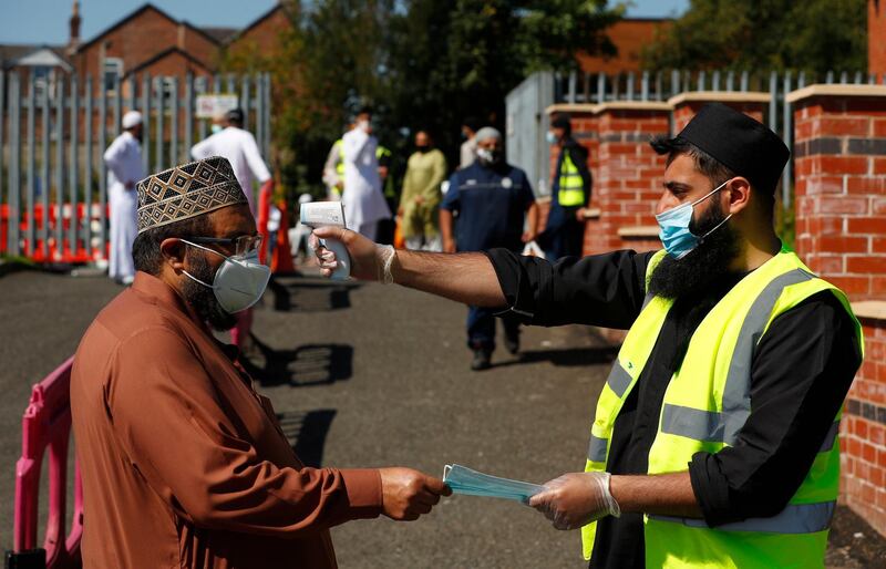 epa08576648 A Jamia Mosque worker distributes face masks and checks the temperature of a man before Friday prayers at North Manchester Jamia Mosque in Manchester, Britain, 31 July 2020. Areas of Greater Manchester have gone back in to lockdown.  EPA/LYNNE CAMERON