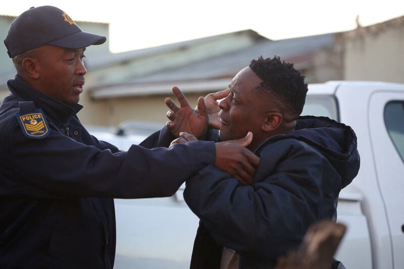 A police officer tries to calm a bereaved relative outside Enyobeni Tavern.  