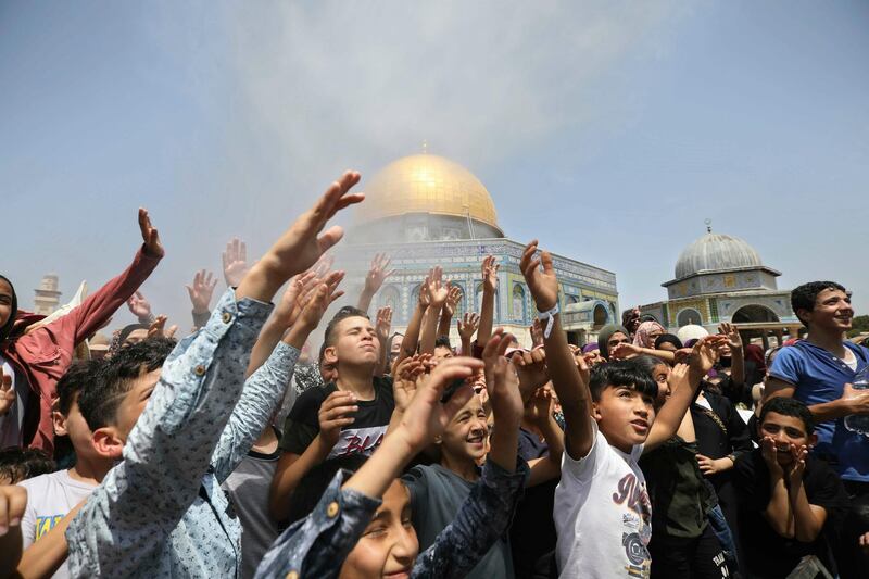 Palestinian youths stand under water sprayed to cool the crowd during the last Friday prayer of the holy month of Ramadan near the Dome of the Rock Mosque in the Al Aqsa Mosque compound in Jerusalem's old city, Friday, May 31, 2019. (AP Photo/Mahmoud Illean)