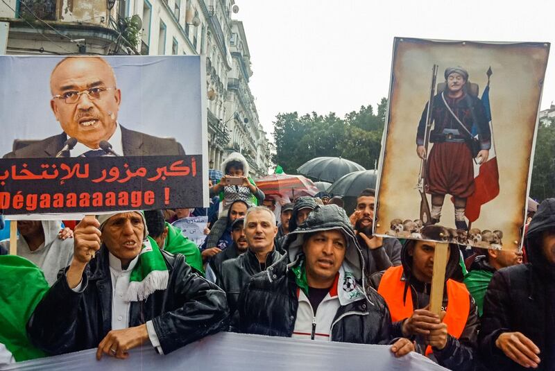 Algerians hold up signs depicting former prime minister Ahmed Ouyahia (R) dressed as a Zouave alongside another showing current PM Noureddine Bedoui with a caption below reading in Arabic "biggest election forger", during an anti-government demonstration in the northeastern city of Annaba, about 570 kilometres west of the capital Algiers and about 100 kilometres east of the border with Tunisia, on April 12, 2019. Algerian protesters gathered for the first Friday protests since the announcement of presidential elections to succeed ousted leader Abdelaziz Bouteflika fearing a ploy by the ruling system to stay in power. / AFP / Bendjama MUSTAPHA
