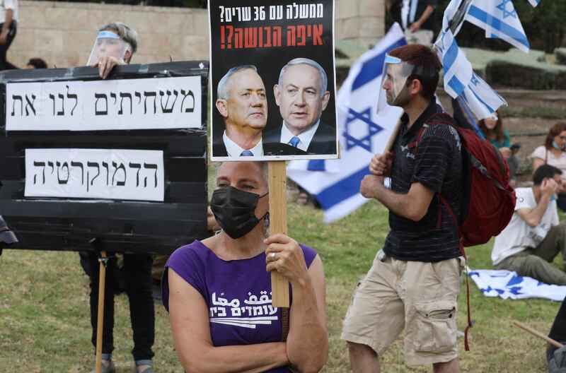 A woman stands on the lawn outside the Knesset (Israel's parliament) in Jerusalem, on May 14, 2020, holding a sign showing the faces of Israeli Prime Minister Benjamin Netanyahu (R) and ex-rival Benny Gantz (L), during a demonstration protesting against the new Israeli government expected to be sworn-in later after nearly 18 months of political gridlock.  / AFP / Menahem KAHANA
