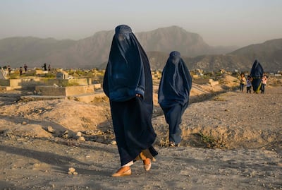 In this picture taken on July 19, 2022, Afghan women wearing burqas walk past a cemetery in Kabul. AFP