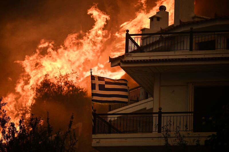 A Greek flag flutters in the wind against a terrifying backdrop of fire in Chasia, near Athens. AFP