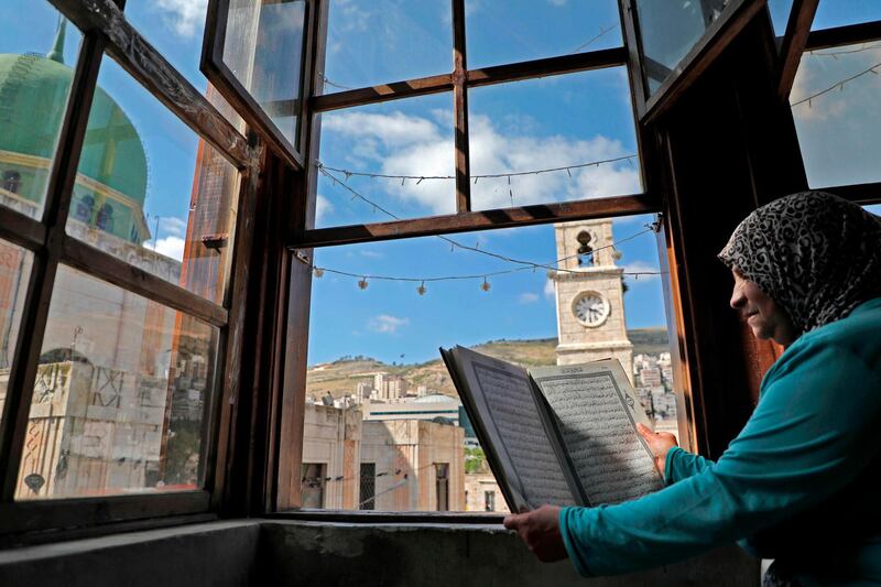 An elderly Palestinian woman reads the Quran at her window overlooking the Manara clock tower and Al Nasr Mosque in the old town of the West Bank city of Nablus. AFP