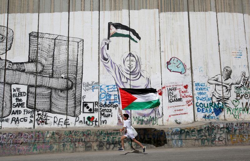 A Participant runs past the Israeli barrier during the annual Palestine Marathon in Bethlehem, in the occupied West Bank,  March 23, 2018. REUTERS/Mussa Qawasma