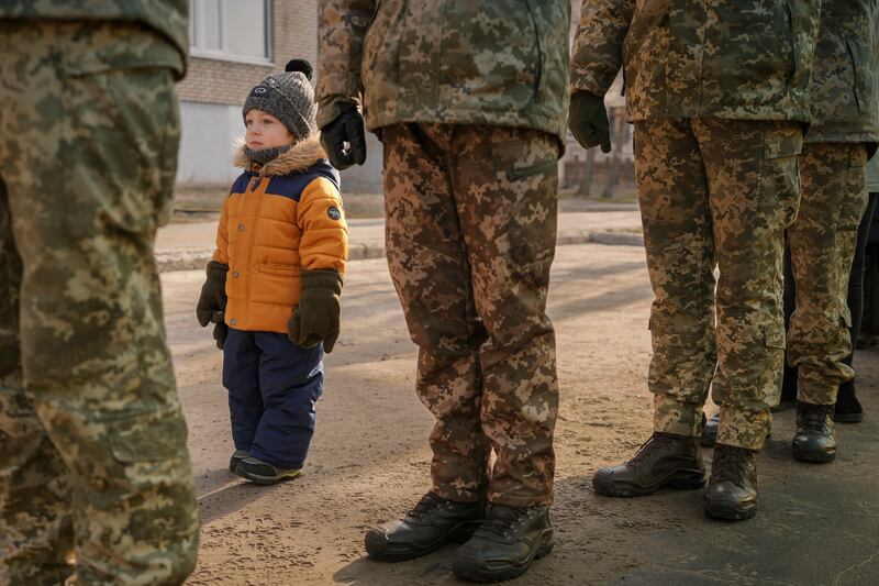 A child copies the position of Ukrainian servicemen standing at attention during the national anthem in Sievierodonetsk, eastern Ukraine. AP