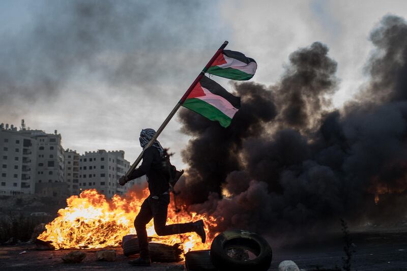 RAMALLAH, WEST BANK - DECEMBER 09:  A Palestinian protester runs past a burning barricade carrying a Palestinian flag during clashes with Israeli border guards near an Israeli checkpoint on December 9, 2017 in Ramallah, West Bank. Protests and clashes continued into a fourth day across Jerusalem and the West Bank following U.S. President Donald Trump's decision to recognize Jerusalem as Israel's capital.  (Photo by Chris McGrath/Getty Images) *** BESTPIX ***