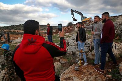 In this Thursday, Dec. 13, 2018 photo, Lebanese villagers smoke a water pipe and take souvenir pictures in front of Israeli excavators, in the southern border village of Mays al-Jabal, Lebanon. As Israeli excavators dig into the rocky ground, Lebanese across the frontier gather to watch what Israel calls the Northern Shield operation aimed at destroying attack tunnels built by Hezbollah. But Lebanese soldiers in new camouflaged posts, behind sandbags, or inside abandoned homes underscore the real anxiety that any misstep could lead to a conflagration between the two enemy states that no one seems to want. (AP Photo/Hussein Malla)