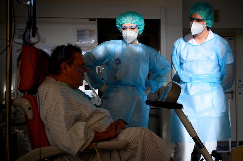 A Swiss army soldier, right, wearing personal protective equipment helps hospital's physiotherapists to treat a Covid-19 patient in the intermediate care units of Geneva University Hospital.  AP