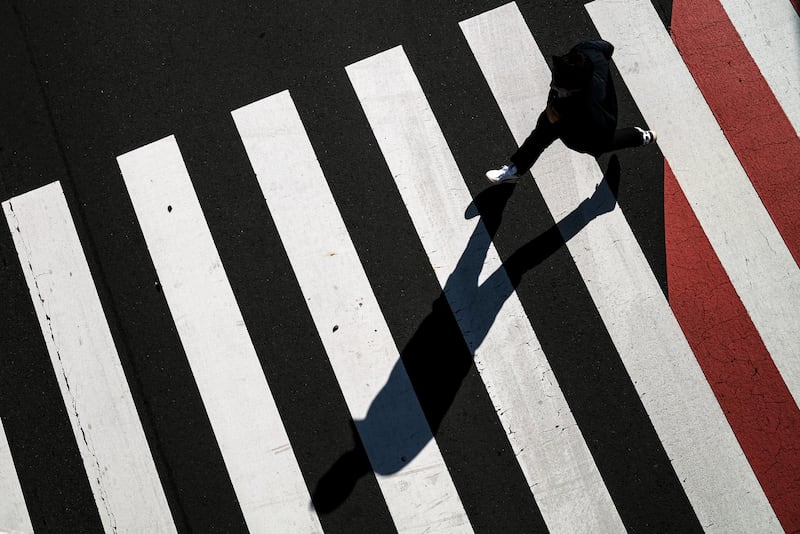 A jogger wearing a protective mask passes through a crosswalk in Tokyo. Japan started emergency measures Sunday in Tokyo, Osaka and two of its neighboring prefectures, closing down bars, karaoke, department stores, theaters and museums and other nonessential businesses and requiring staying home and other preventive measures for the residents until May 11. AP Photo
