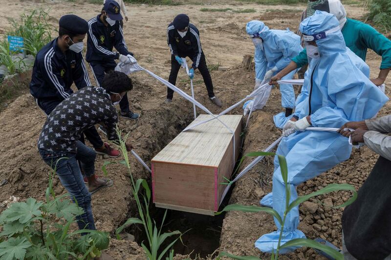 Relatives, graveyard workers and volunteers lower the coffin of a coronavirus victim during a funeral at a graveyard in New Delhi. AFP