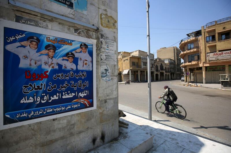 An Iraqi man rides his bicycle past a poster, urging people to stay alert, in central Baghdad, during a nationwide lockdown to stem the spread of coronavirus.  AFP