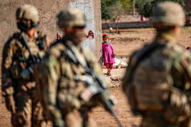 A little girl peeps around the corner of a building while US soldiers patrol an area near Tal Alo.   AFP