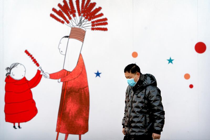 A man wearing a face mask to protect against the spread of the coronavirus walks past a mural at a shopping and office complex in Beijing. New cases of local transmission in China are continuing to fall with just several dozen announced on Friday, even as the country's annual Lunar New Year travel push gets underway. AP Photo