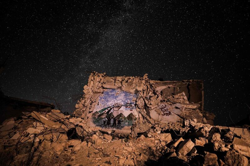 This long-exposure picture taken shows a view of the Milky Way galaxy rising in the sky above the rubble of a building in the town of Ihsim in Syria's rebel-held northwestern Idlib province, with a graffiti depicting silhouettes of children with roots standing before a fist clenching a flag of the Syrian opposition with apples instead of stars.  AFP