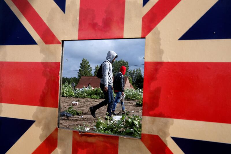 Migrants are reflected in a mirror bordered with the Union Jack as French police officers dismantle a makeshift shelter camp in Calais, France. Reuters