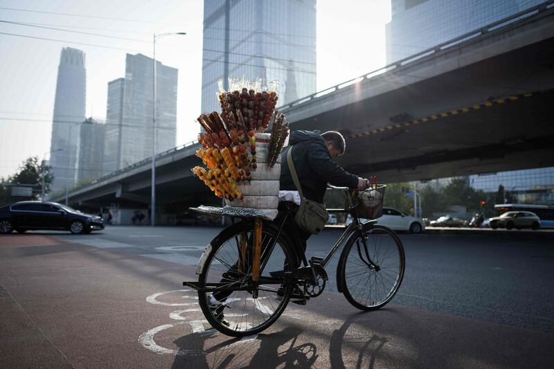 A vendor pushes his bicycle across a street in Beijing's central business district on October 18, 2019. / AFP / WANG Zhao
