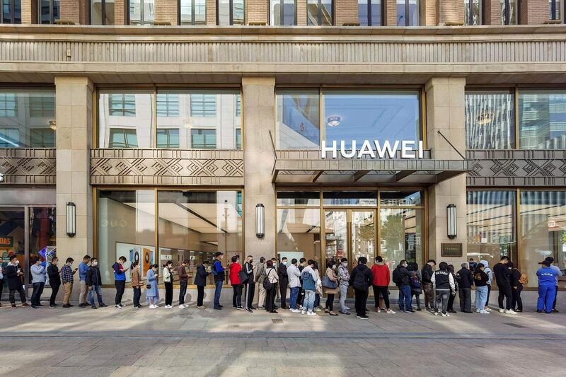 People wearing masks wait in line in front of Huawei’s flagship store for pre-sales of the newly launched Huawei Mate40 mobile phone series in Shanghai on October 23, 2020. / AFP / STR
