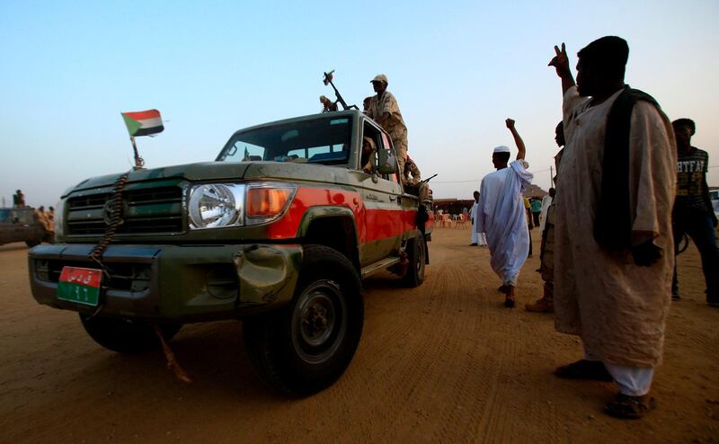 A technical (pickup truck mounted with a machine gun turret) carrying members of Sudan's Rapid Support Forces (RSF) paramilitaries drives by a man flashing the victory gesture during a rally in the village of Qarri, about 90 kilometres north of Khartoum.  AFP