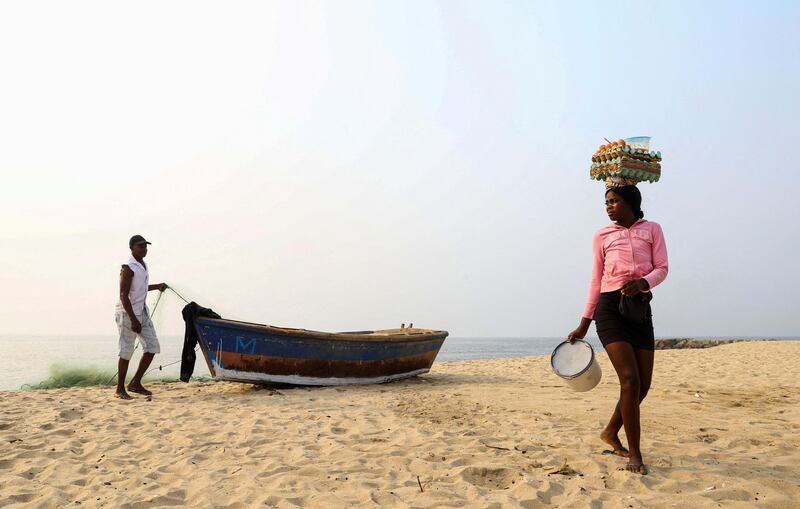 A woman selling eggs passes a man preparing to launch his boat in Luanda, Angola. Reuters