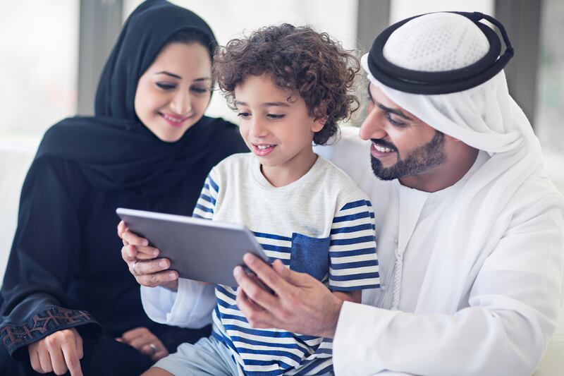 Middle Eastern parents teaching how to use the digital tablet to their son, kid is seated on the lap of his father while mother is pointing out the digital tablet.