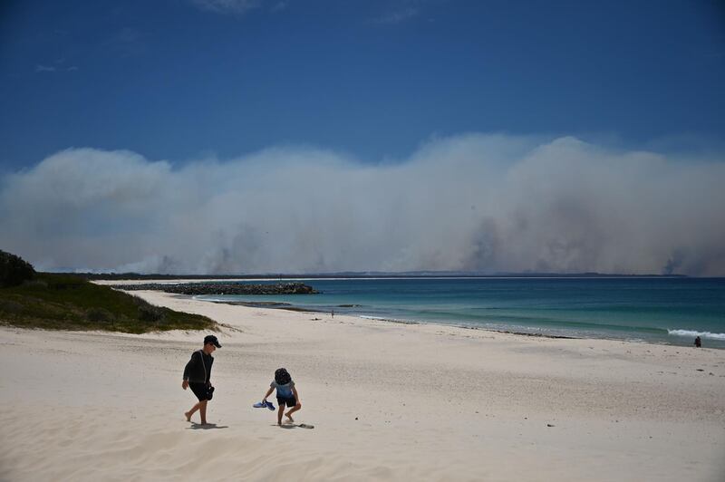 Bushfires burn in the distance as children play on a beach in Forster, 300km north of Sydney, as firefighters try to contain dozens of out-of-control blazes that are raging in the state of New South Wales. AFP