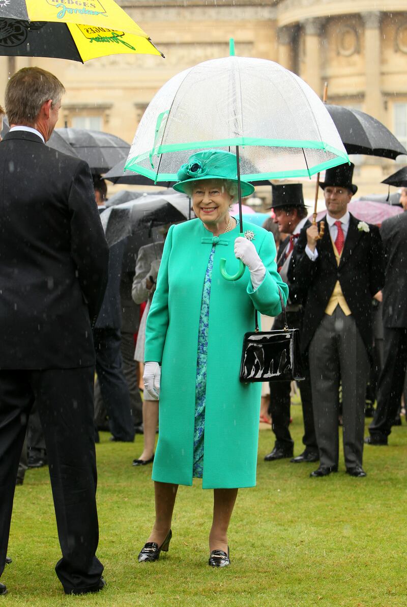 Queen Elizabeth II, wearing green, shelters from the rain during a garden party at Buckingham Palace on July 19, 2011 in London, England. Getty Images