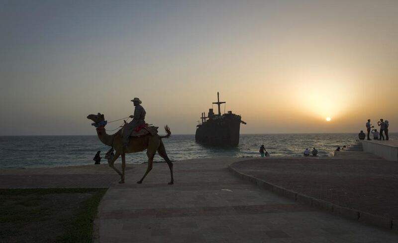 A man rides his camel along the coast, in front of the beached Greek ship Moula F, during sunset off Kish Island. Reuters