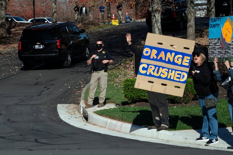 In this image made through the window of the press vehicle accompanying the motorcade carrying President Donald Trump, people hold signs at the entrance of Trump National Golf Club. AP