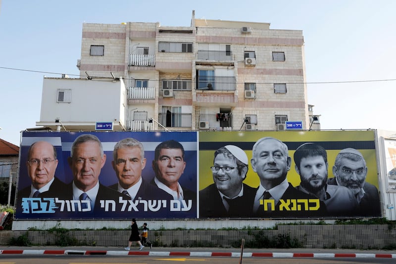 epa07451282 Israelis walk past an election billboard placed by the centrist Israeli Blue and White alliance parties featuring their candidate for Prime Minister, Benny Gantz (L panel 2-L) alongside a panel showing the Likud party (R) with Prime Minister Benjamin Netanyahu and extreme right-wing members of the Union of the Right praty Netanyahu's coalition partners, in Tel Aviv, Israel, 20 March 2019. On the right side the Hebrew translates, 'Kahana Lives' and on the left reads, 'People of Israel live Blue and White'. Israelis go to general elections on 09 April 2019.  EPA/ABIR SULTAN