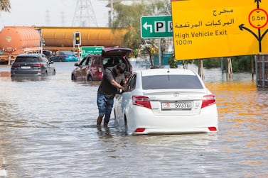 A motorist helped by friends pushes his car out of a flooded street in Dubai. Ruel Pableo / The National